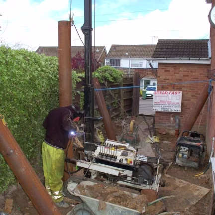 Underpinning specialists installing case‑driven piles with welding beside a residential foundation in Essex